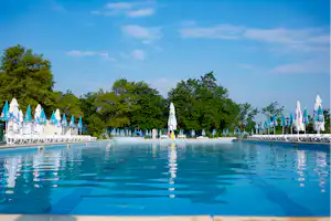 Blauer Camping-Pool mit Spiegelungen, Reihe blauer Sonnenschirme und Bäume im Hintergrund.