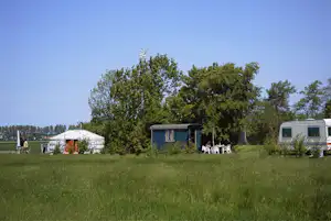 Wohnwagen und Zelt auf grünem Campingplatz, im Hintergrund Bäume und ein weiteres Mobilheim mit Sitzbereich.