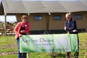 Zwei Personen stehen vor einem Zelt und halten ein grünes Banner mit Text „Aan het Diepje“.