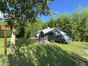Wohnmobil auf einem Campingplatz-Stellplatz mit Vorzelt, Tisch und Stühlen unter Bäumen, daneben ein Schild mit 19/20.