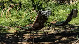 Zwei Campingliegen mit Metallgestell im Schatten, umgeben von grünem Garten und Büschen.