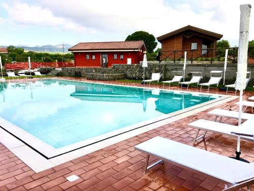 Schwimmbad mit türkisfarbenem Wasser, Sonnenliegen und Ziegelterrasse vor roten Gebäuden und einem Holzpavillon.