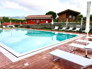 Schwimmbad mit türkisfarbenem Wasser, Sonnenliegen und Ziegelterrasse vor roten Gebäuden und einem Holzpavillon.