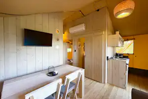 Innenansicht eines Wohnwagens mit Küchenzeile, Esstisch und weißen Stühlen, Holzverkleidung und Flachbildschirm an der Wand.