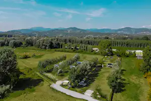 Luftaufnahme eines Campingplatzes mit Wohnwagen und Zelten, schmalem Weg durch die Wiesen und Blick auf bewaldete Hügel.