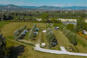 Luftaufnahme eines Campingplatzes im Tal mit mehreren Stellplätzen, Wohnwagen und Bungalows, umgeben von Wiesen und Bäumen.