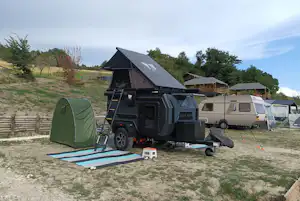 Wohnmobil mit ausklappbarem Dachzelt und grünem Zelt auf dem Campingplatz, im Hintergrund weitere Wohnwagen und Bäume.