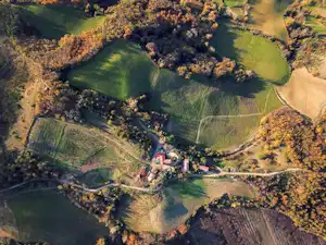 Luftaufnahme eines Campingplatzes mit Wiesen, Wegen und einem kleinen Fluss im Tal, umgeben von Bäumen und Feldern.