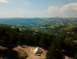 Zelt auf einem Campingplatz inmitten von Bäumen, Blick über grüne Hügel und Täler in die Ferne.