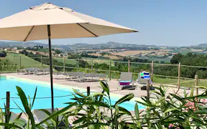 Pool und Holzterrasse mit Sonnenliegen, Sonnenschirm und Blick über grüne Hügel in die Ferne.