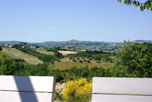 Blick von einer Terrasse auf hügelige Landschaft mit Feldern, Wäldern und Häusern in der Ferne.