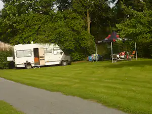 Wohnmobil auf einem Stellplatz mit Vorzelt, Campingstühlen und Tisch unter Bäumen auf einer grünen Wiese.