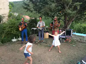 Musikgruppe mit Gitarren und Keyboard auf dem Campingplatz, Kinder tanzen auf dem Weg vor dem Zeltbereich und Bäumen.