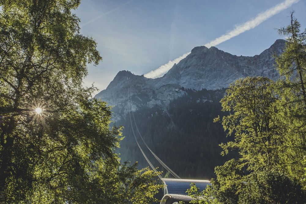Bergpanorama der Alpen zwischen Bäumen, im Vordergrund ein Campingdach mit blauem Streifen und Straße im Tal.