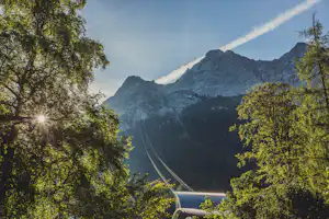 Bergpanorama der Alpen zwischen Bäumen, im Vordergrund ein Campingdach mit blauem Streifen und Straße im Tal.