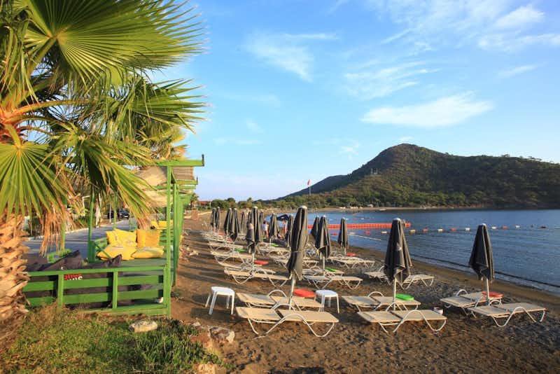 Aktur Datça Mocamp  -  Campingplatz am Strand mit Sonnenschirmen und Liegestühlen