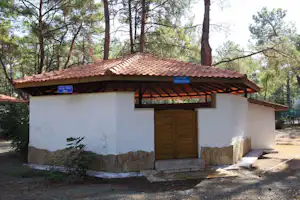 Campinghaus mit Veranda und Holz-Türen, weißer Wand und Ziegeldach im Wald mit Bäumen im Hintergrund.