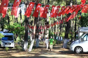 Campingplatzweg im Wald mit roten Fähnchen, Wohnmobilen und zwei Personen zwischen den Bäumen.