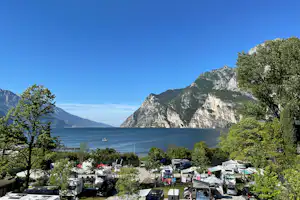 Campingplatz mit Stellplätzen und Wohnmobilen, Blick auf den See und die Berge, umgeben von Bäumen.