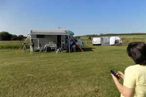 Wohnmobil mit Vorzelt und Campingstühlen auf einer grünen Wiese, daneben Zelt und Fahrrad am Stellplatz.