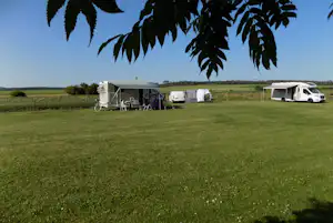 Wohnmobil und Zelte auf einer Campingwiese, Fahrräder am Stellplatz, im Hintergrund weitere Fahrzeuge und Felder.