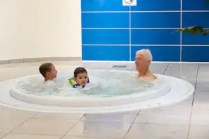 Mann und Kind im Whirlpool im Innenbereich, weiße Fliesen und blaue Wandkacheln im Hintergrund.