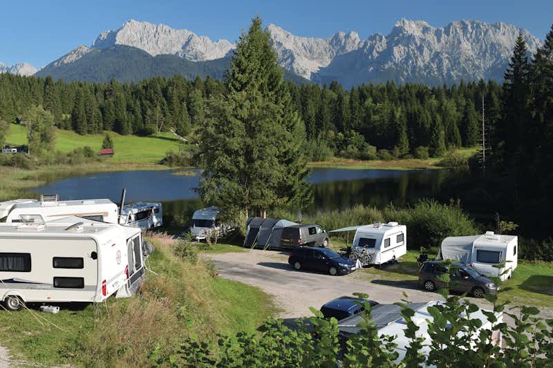 Alpen-Caravanpark Tennsee - Wohnwagen und Wohnmobile auf Stellplätzen vor einem See mit den Alpen im Hintergrund