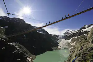 Alpencamping - Brücke mit Wanderern darauf in den Alpen über einem Bergsee
