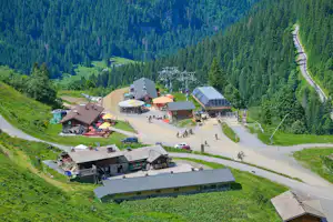 Alpen-Campinganlage im Tal mit mehreren Gebäuden, Wegen und Stellplätzen, umgeben von grünen Wiesen und hohen Bergen.