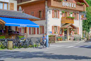 Hotelgebäude am Campingplatz-Eingang mit Fahrrädern am Straßenrand und Sonnenschirm vor der Terrasse.