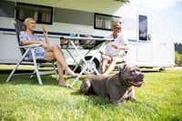 Alpsee Camping - Camperpaar mit Hund vor ihrem Wohnwagen in der Sonne