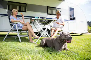 Alpsee Camping - Camperpaar mit Hund vor ihrem Wohnwagen in der Sonne