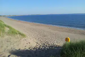 Sandstrand mit Dünen und Gras am Rand, Blick auf das Meer und die Küste in der Ferne.