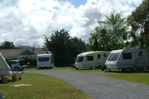Wohnmobile auf einem Campingplatz, Kiesweg und Rasenflächen, Bäume und Wohnhäuser im Hintergrund.