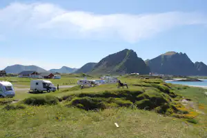 Campingwiese mit Wohnwagen und Autos, im Hintergrund Berge und das Meer, daneben ein schmaler Weg.