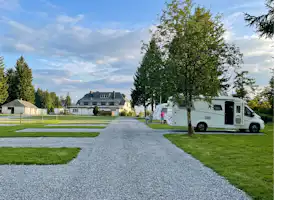 Wohnmobil auf einem Campingplatz am Weg, mit Rasenflächen und Bäumen, im Hintergrund Häuser und ein Zaun.