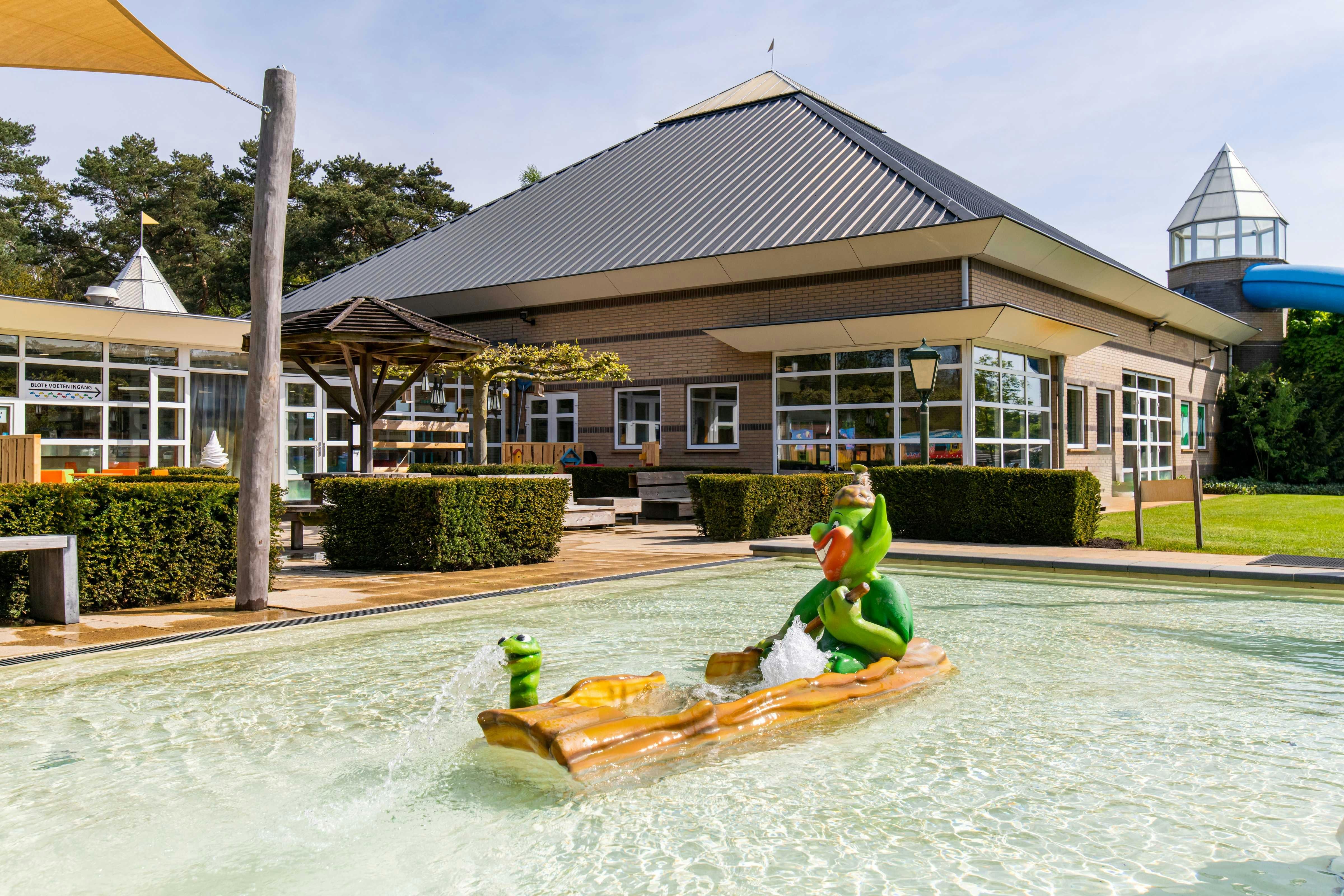 Schwimmbecken mit aufblasbaren Schwimmringen, im Hintergrund ein Campinggebäude mit überdachter Terrasse und Glasfront.