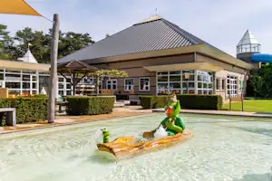 Schwimmbecken mit aufblasbaren Schwimmringen, im Hintergrund ein Campinggebäude mit überdachter Terrasse und Glasfront.