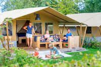 Camping De Zandhegge - Glampingzelt auf dem Campingplatz vor dem eine Familie die Sonne genießt