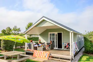 Ardoer Camping De Zwinhoeve - Mobilheim vom Campingplatz mit Sitzmöglichkeit auf der Veranda und Picknicktisch auf grüner Wiese
