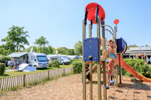 Ardoer Camping Duinoord aan Zee - Kind auf dem Spielplatz vom Campingplatz, Wohnwagen- und Zeltstellplatz im Hintergrund