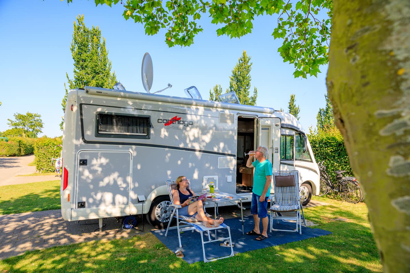 Ardoer Camping Westhove - Camper sitzen vor dem Wohnmobil im Schatten der Bäume