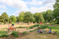 Ardoer Comfortcamping De Bosgraaf  - Kinder mit Fahrrädern am Spielplatz vom Campingplatz im Grünen