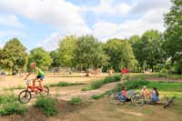 Ardoer Comfortcamping De Bosgraaf  - Kinder mit Fahrrädern am Spielplatz vom Campingplatz im Grünen