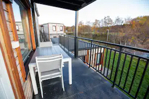 Balkon mit zwei weißen Stühlen und Tisch, Blick auf einen Wohnwagen und Bäume am Campingplatz.