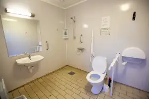 Camping-Badezimmer mit Waschbecken, Toilette und Dusche, hell gefliestem Boden und Wandarmaturen.