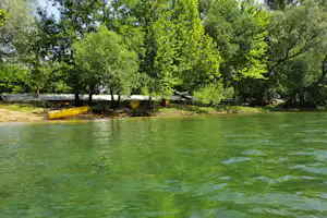 Grünes Wasser im Pool, gelbe Schlauchboote am Ufer, Bäume und Sitzbänke im Hintergrund.