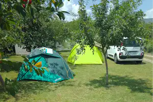 Zelt im grünen Garten auf dem Campingplatz, daneben ein weißer Wohnwagen und ein Auto auf dem Stellplatz.