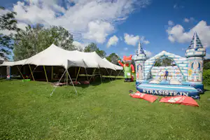 Weiße Zelte auf einer grünen Campingwiese, daneben eine große Hüpfburg mit bunten Motiven.