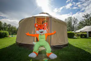 Beiges Zelt im Campinggarten, davor eine Kinderfigur im Kostüm auf dem Rasen, im Hintergrund weitere Zelte und Bäume.